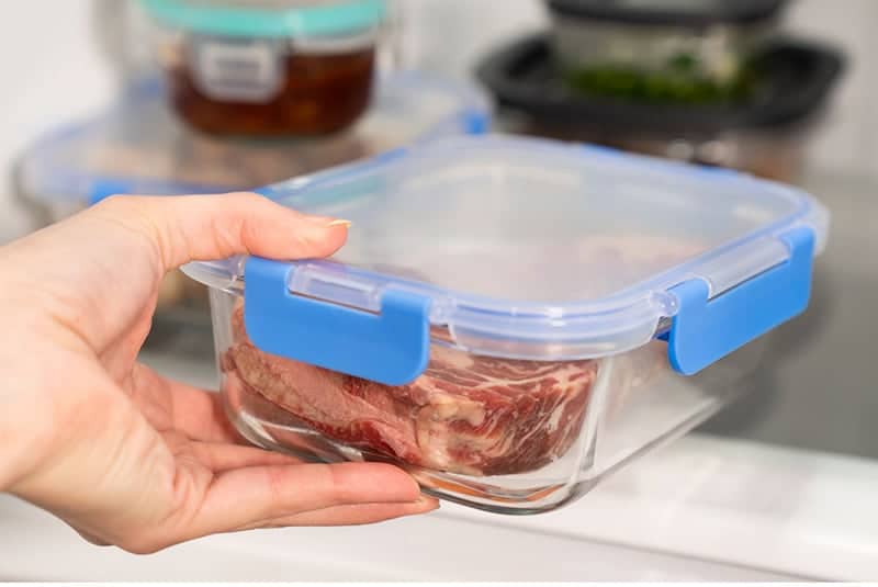 Grass fed beef in a glass container being placed into the refrigerator